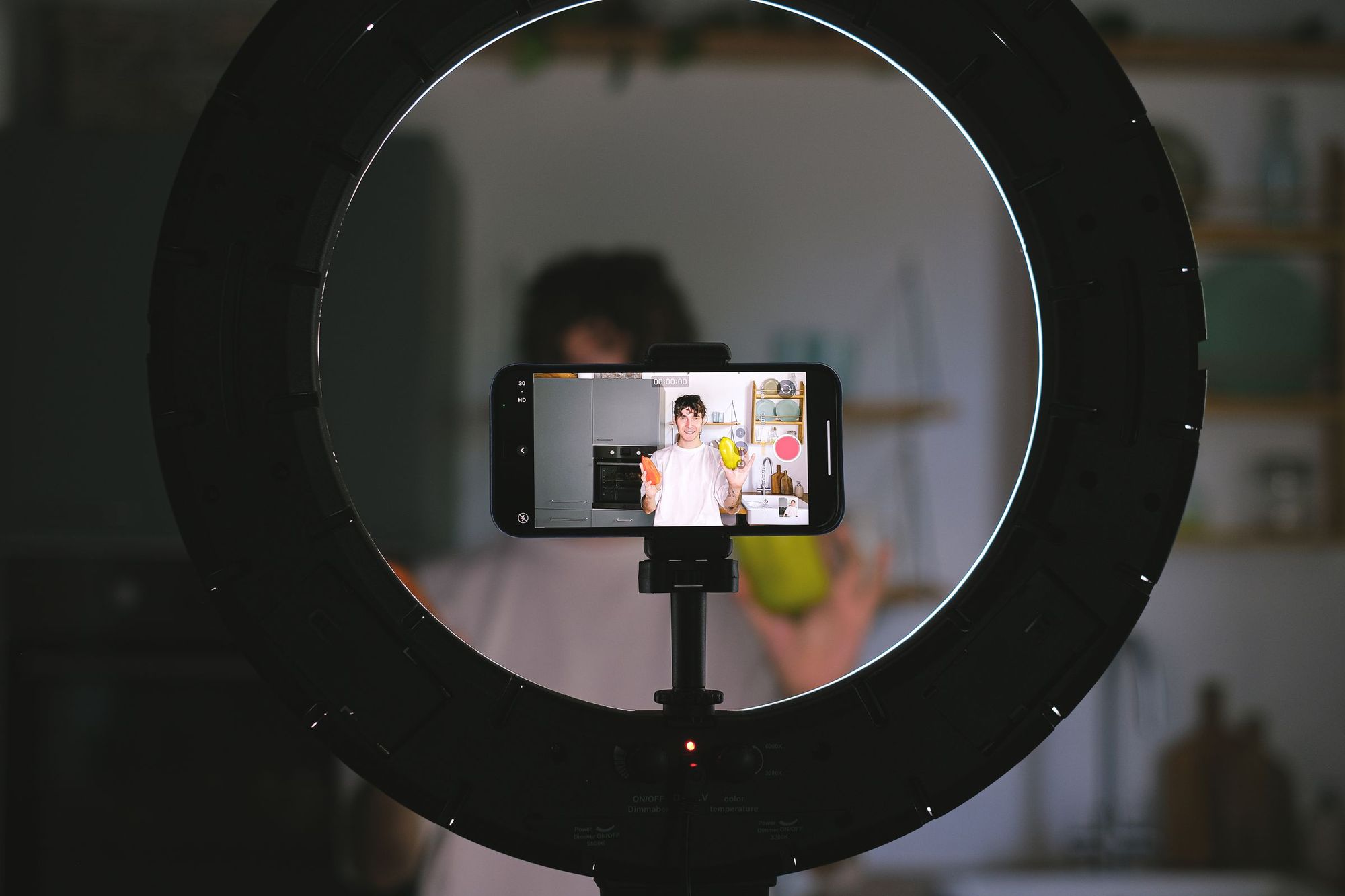 Smartphone in einem Ringlicht filmt eine Person beim Kochen